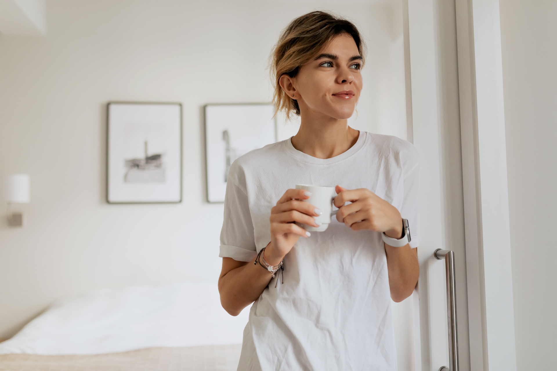 A woman standing peacefully in her sunlit new apartment, holding a mug of tea, surrounded by soft pastel linens and unpacked boxes